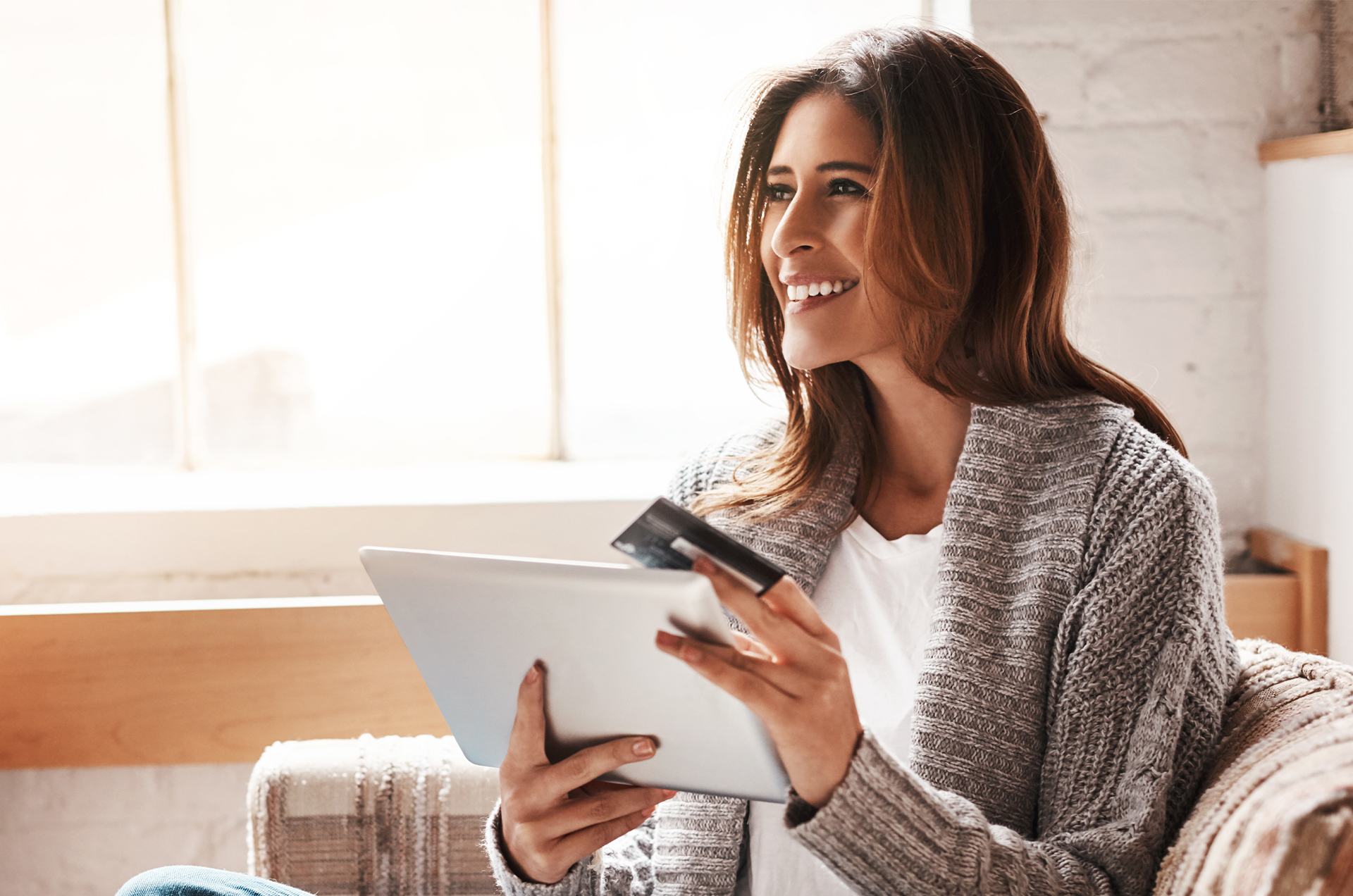 Woman in a sweater holding a tablet and a credit card